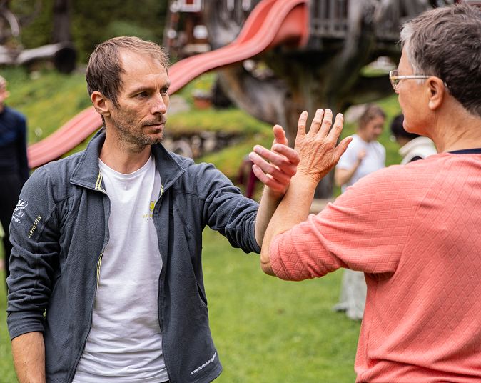 A group of people practicing outdoor martial arts with focused expressions. A slide and trees are visible in the background.