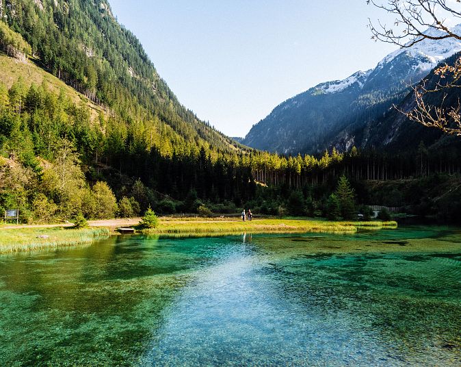 The crystal-clear, turquoise-blue Blausee lake in Neukirchen, surrounded by lush forests and majestic mountains beneath a blue sky. A picturesque, peaceful Alpine landscape.