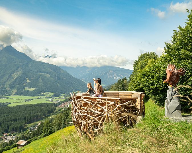 Aussichtspunkt mit Personen in der Wildkogel-Arena, umgeben von Bergen und grünen Tälern in den Alpen, unter einem blauen Himmel mit wenigen Wolken.
