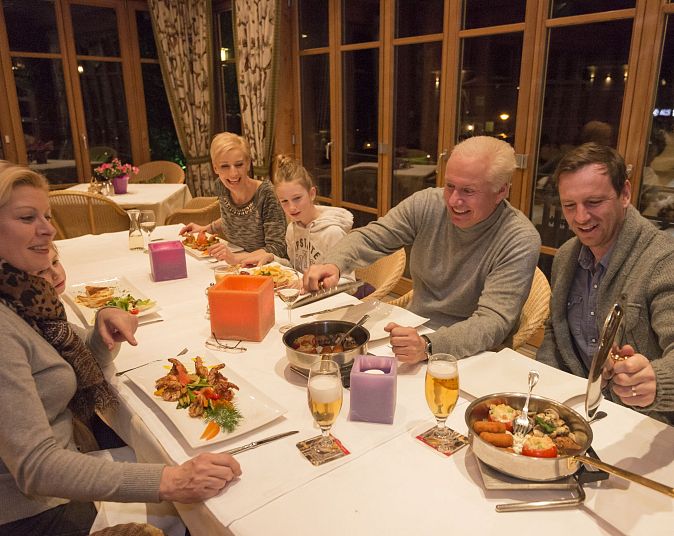 Eine Familie sitzt in einem gemütlichen Restaurant an einem Tisch, genießt ein gemeinsames Essen mit Getränken. Lächelnde Gesichter und herzliche Atmosphäre.