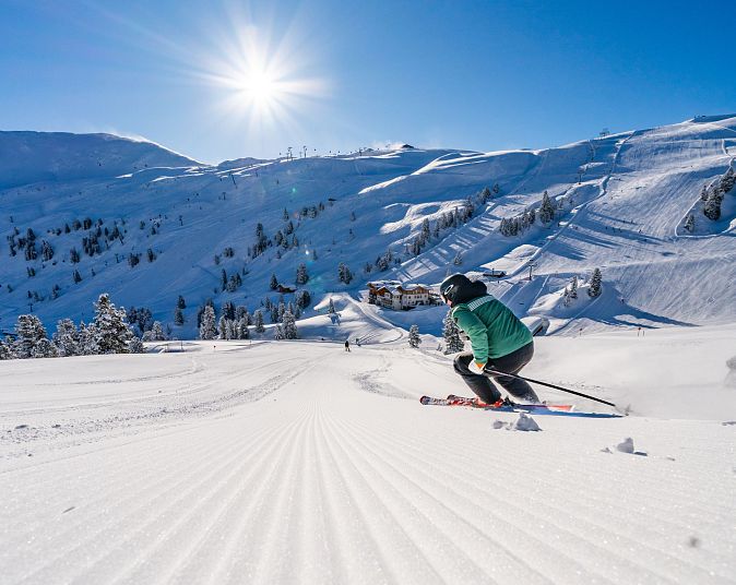 Een skiër glijdt elegant over een pas geprepareerde piste in de Wildkogel-Arena, terwijl de zon achter de met sneeuw bedekte bergen schijnt.