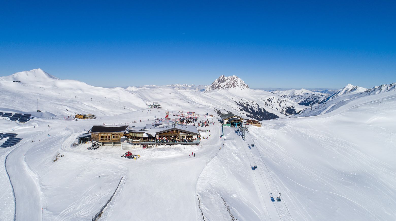 Een sneeuwlandschap met een skicentrum in de bergen, omringd door besneeuwde hellingen en een heldere blauwe lucht.