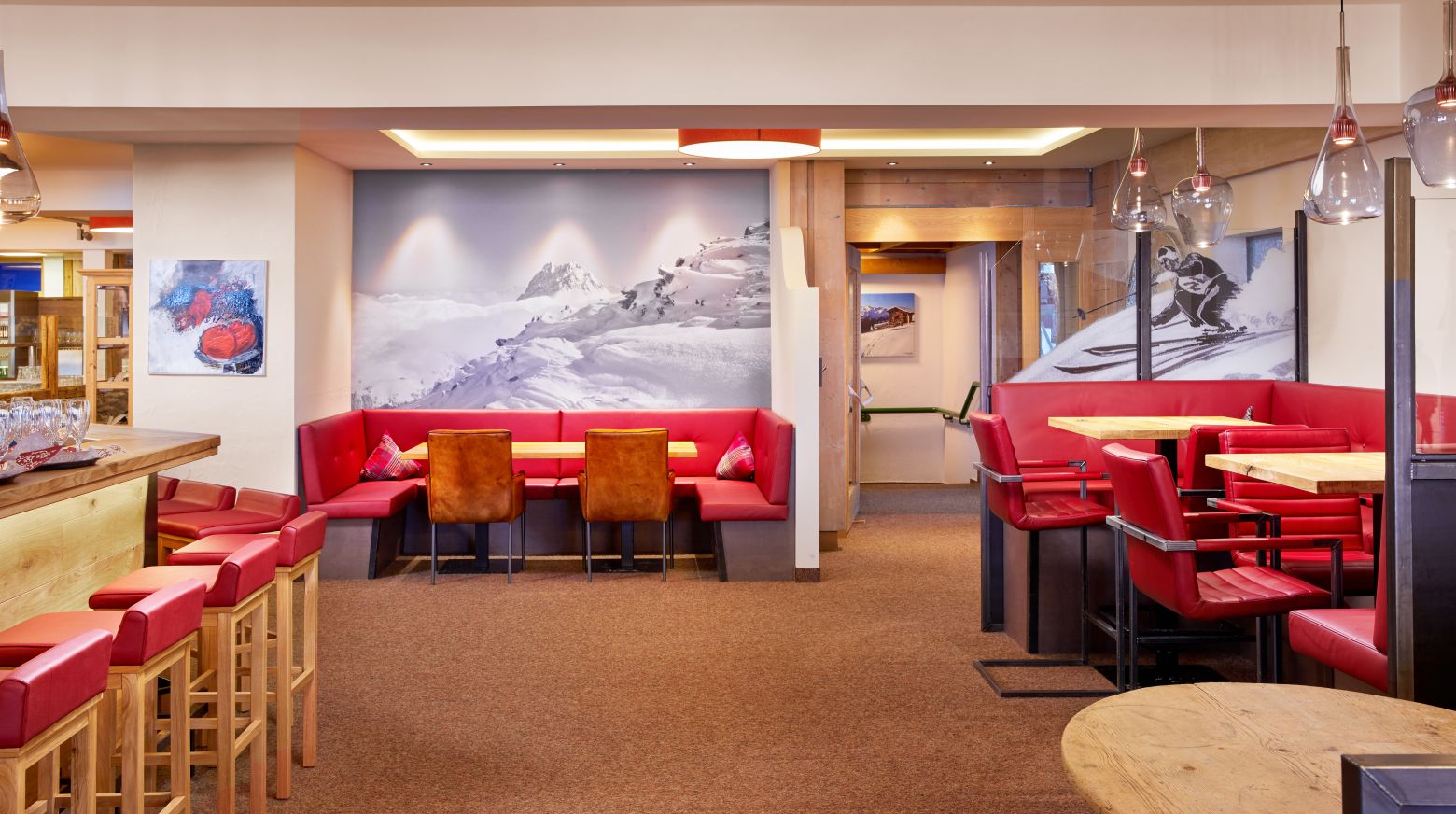 Gemütliches Restaurant mit roter Polsterung, Holzmöbeln und Skimotiven an den Wänden. Die Beleuchtung ist warm und schafft eine einladende Atmosphäre.