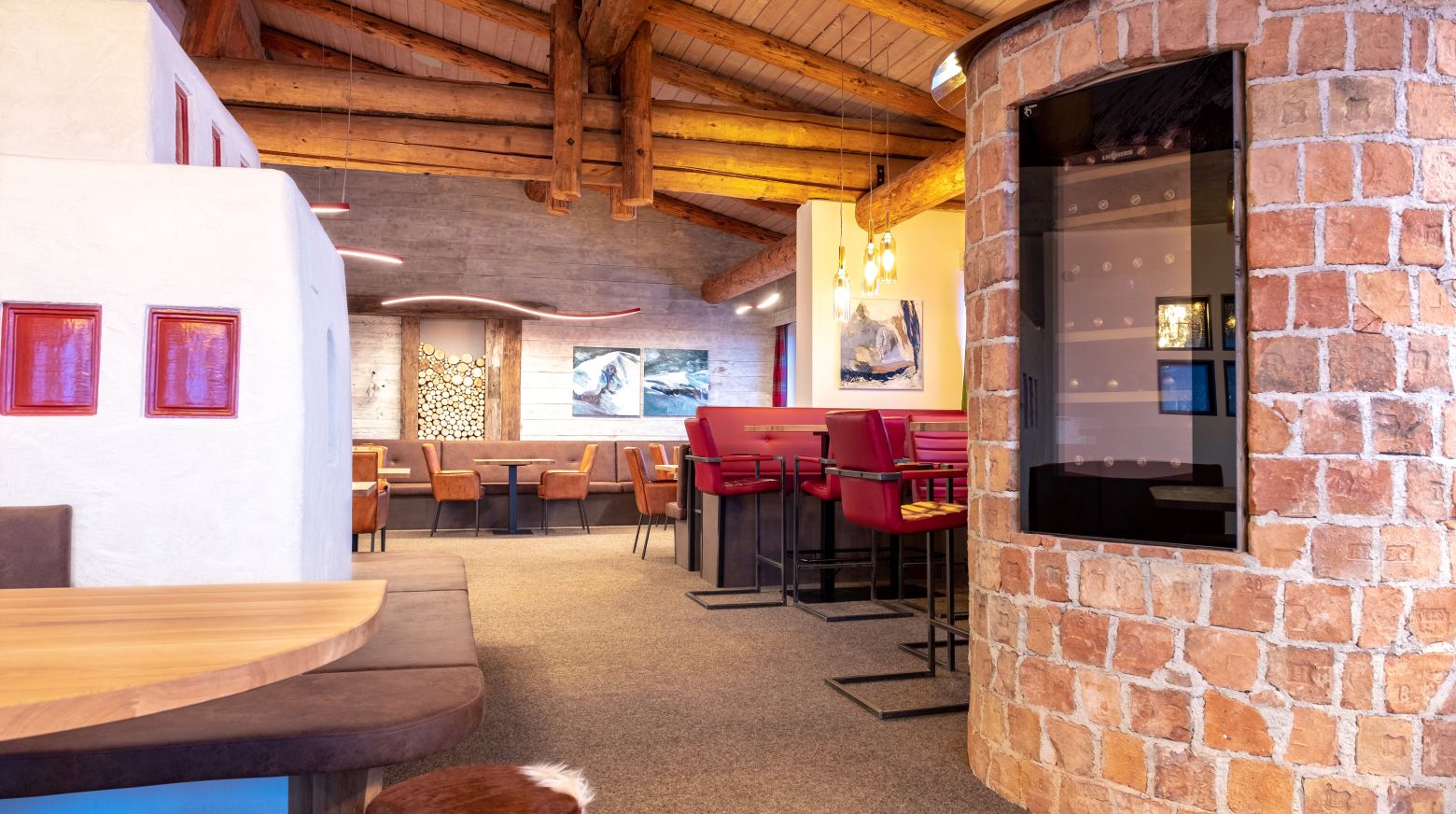 Gemütliches Restaurant mit Holzbalkendecke, roten Barhockern und gemauertem Kamin. Warme Beleuchtung und Holztische schaffen eine einladende Atmosphäre.