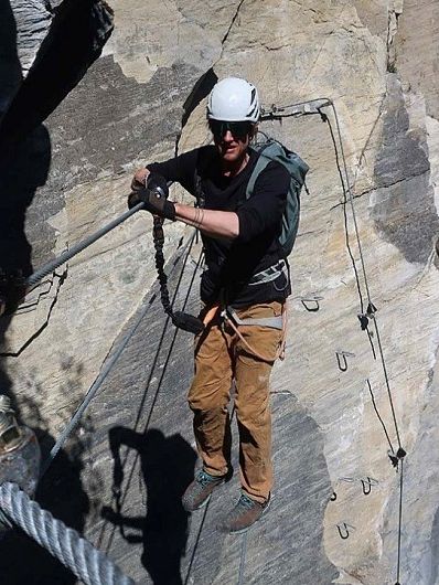 Person klettert gesichert auf einem Via Ferrata durch eine steile Felswand. Der Kletterer trägt Helm, Handschuhe und Kletterausrüstung.