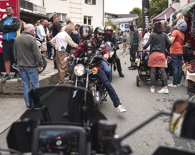 Belebte Straßenszene bei einem Motorradtreffen mit dicht gedrängten Menschen, Ständen und Motorrädern in einer kleinstädtischen Umgebung an einem sonnigen Tag.
