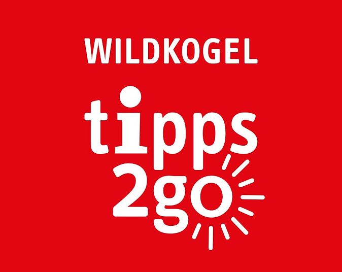 Rotes Schild mit weißem Text: "Wildkogel tipps 2go" und einem stilisierten Sonnensymbol. Der Hintergrund ist kräftig rot, der Text mittig platziert.