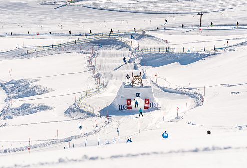 Bild zeigt die Funslope und den Familypark im Skigebiet Wildkogel. Verschneite Pisten mit Schanzen und Kurven, umgeben von Skifahrern unter klarem, blauem Himmel.