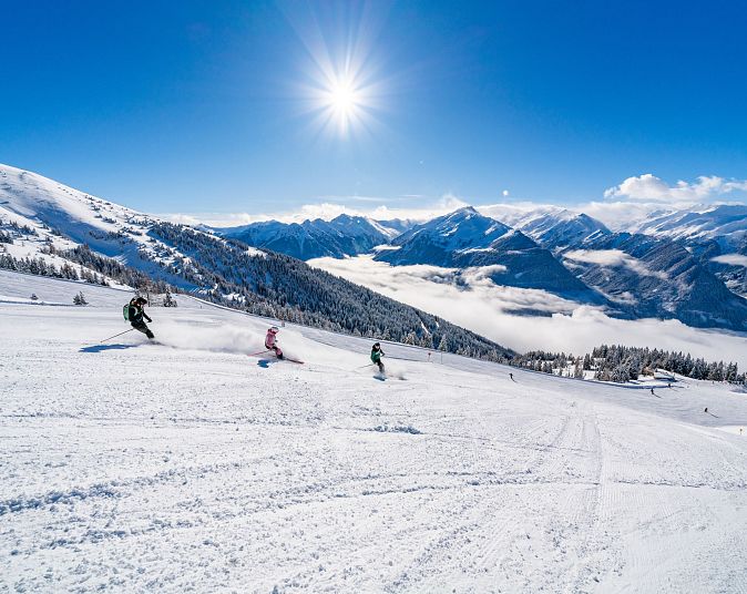 Skigebiet in der Wildkogel-Arena mit strahlendem Sonnenschein und Bergen im Hintergrund. Skifahrer genießen die weiten, schneebedeckten Pisten.