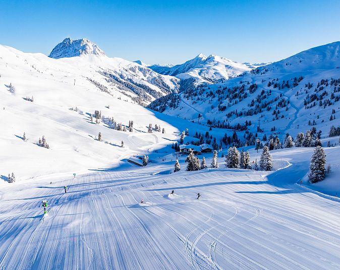 Een prachtig sneeuwlandschap in de bergen met skiërs op de besneeuwde hellingen onder een heldere blauwe hemel.