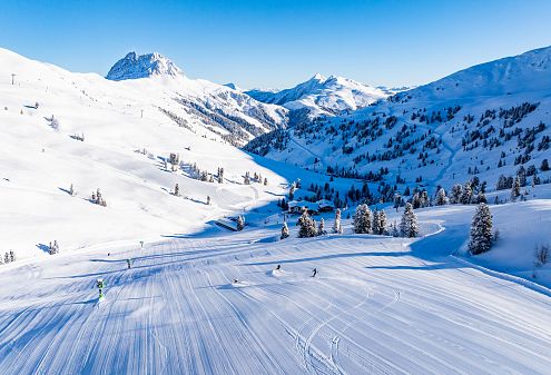 Een prachtig sneeuwlandschap in de bergen met skiërs op de besneeuwde hellingen onder een heldere blauwe hemel.