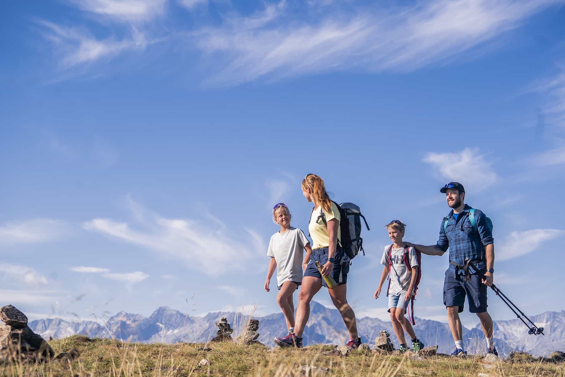 Veselá rodina si užívá túru ve vysokohorské oblasti Wildkogel. Za slunečného počasí a s panoramatickým výhledem na Vysoké Taury tráví aktivní rodinný čas v přírodě – ideální pro letní dovolenou s dětmi v Rakousku.