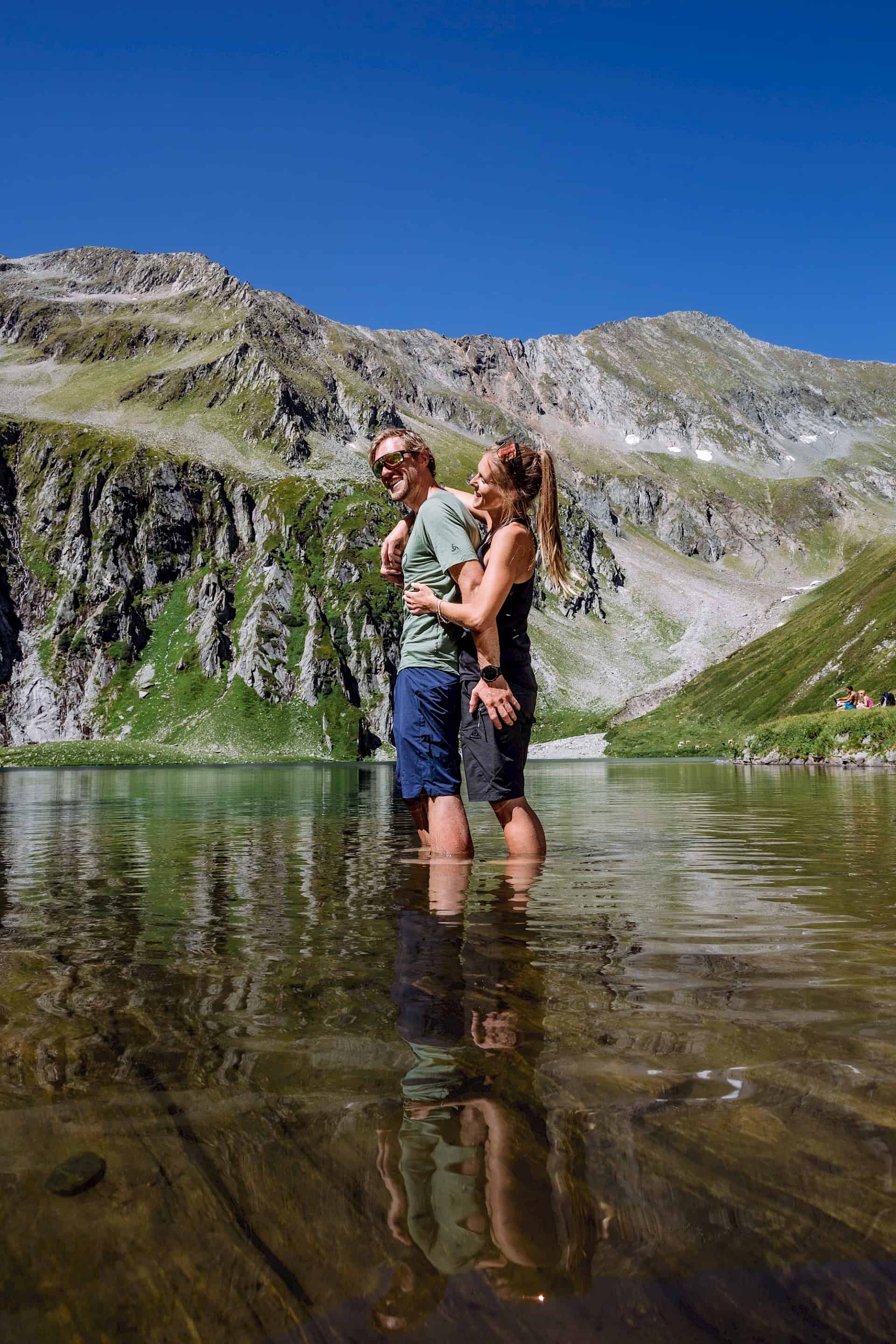 Ein Paar steht lachend im klaren Wasser eines Bergsees in der Wildkogel-Arena – erfrischende Abkühlung nach einer Wanderung inmitten der alpinen Landschaft der Hohen Tauern.