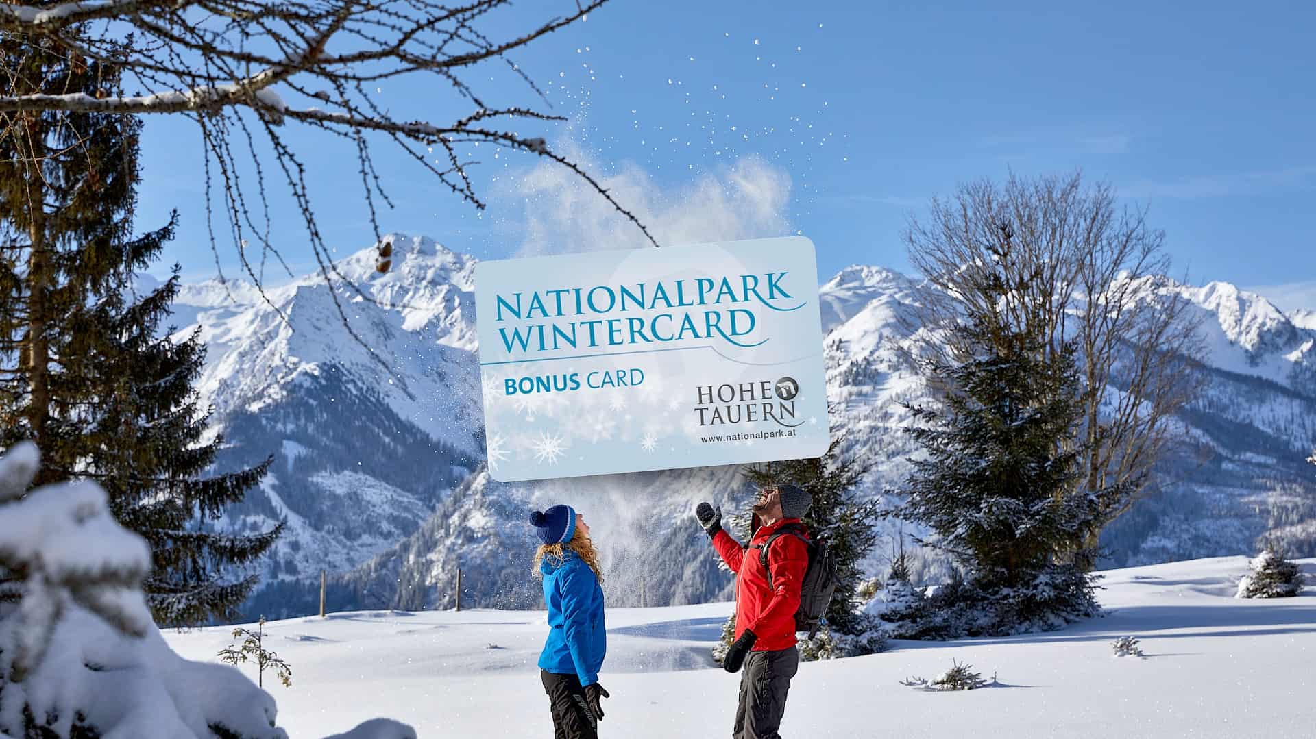 Two winter hikers in the snow-covered Hohe Tauern National Park enjoying the Nationalpark WinterCard Bonus Card with a stunning alpine backdrop.