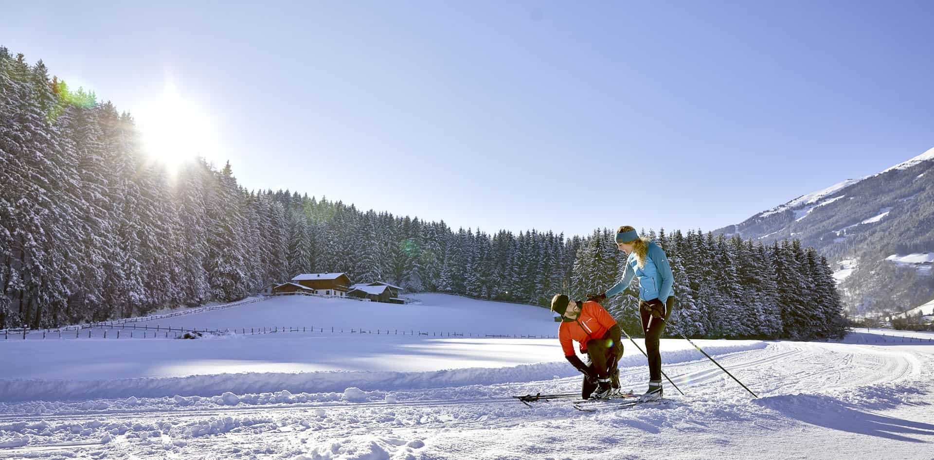 Běžecké lyžování v Bramberg am Wildkogel – sportovní pár si užívá slunečnou zimní krajinu na čerstvě upravené stopě v rekreační oblasti Národního parku Vysoké Taury.