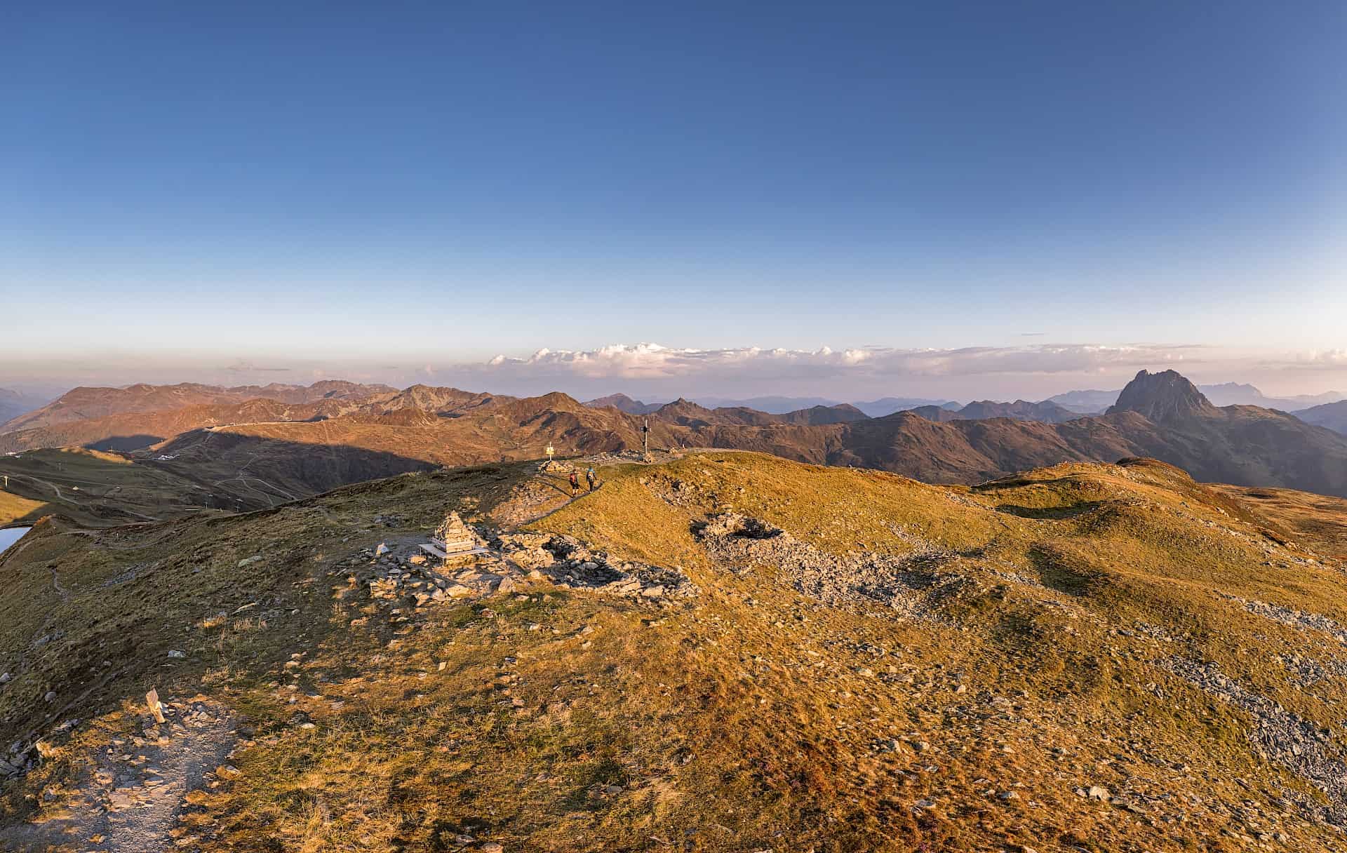 Panoramatický výhled z vrcholu Wildkogel s impozantním pohledem na Großer Rettenstein ve zlatém večerním světle Wildkogel Areny Neukirchen & Bramberg.