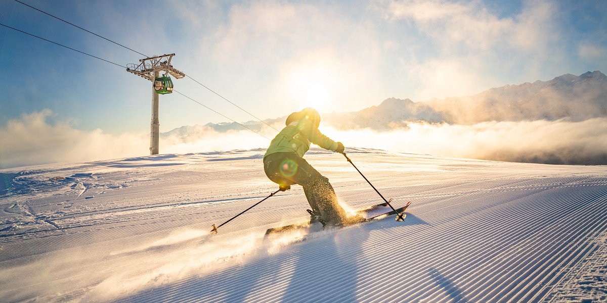 Skifahrer auf frisch präparierter Piste in der Wildkogel-Arena bei Sonnenaufgang – Winterurlaub in den österreichischen Alpen mit Blick auf verschneite Berggipfel und Smaragdbahn. uk-cover