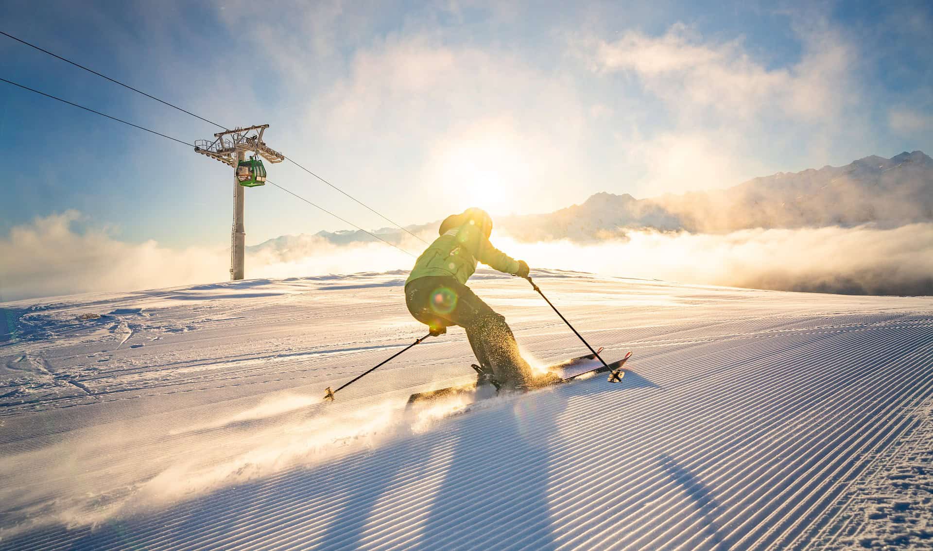 Skifahrer auf frisch präparierter Piste in der Wildkogel-Arena bei Sonnenaufgang – Winterurlaub in den österreichischen Alpen mit Blick auf verschneite Berggipfel und Smaragdbahn.