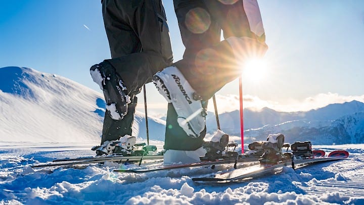 Lyžařské boty na čerstvě upravené sjezdovce ve Wildkogel Areně s panoramatickým výhledem na zasněžené Alpy při východu slunce – dokonalý začátek lyžařského dne v Salcbursku.