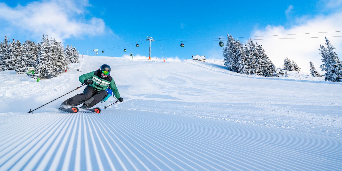 Dynamischer Skifahrer auf perfekt präparierter Piste in der Wildkogel-Arena bei strahlendem Sonnenschein und frischem Pulverschnee. uk-cover