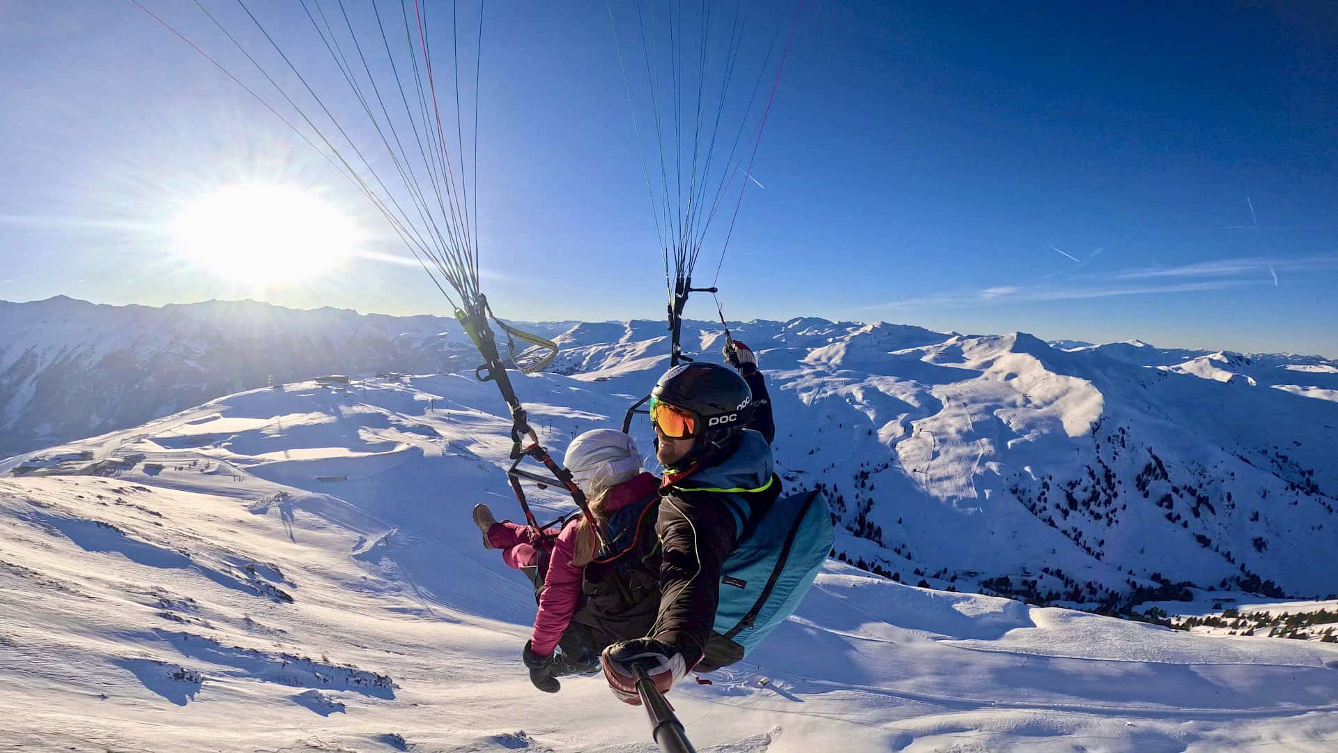 Zimní tandemový paragliding nad zasněženou Wildkogel Arenou – dobrodružství a alpské panorama za jasného slunečného dne.