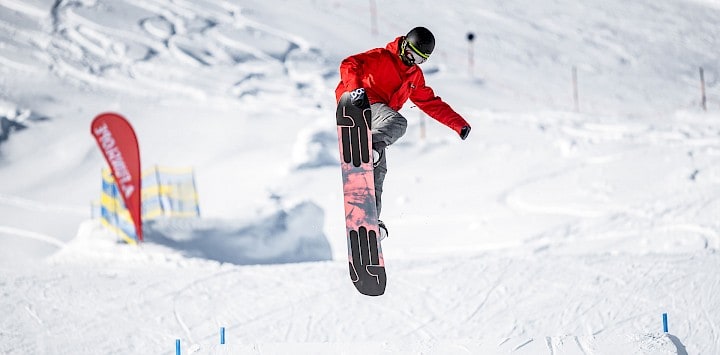 Snowboardista skáče přes překážku ve snowparku Wildkogel Areny za slunečného počasí a ideálních sněhových podmínek.