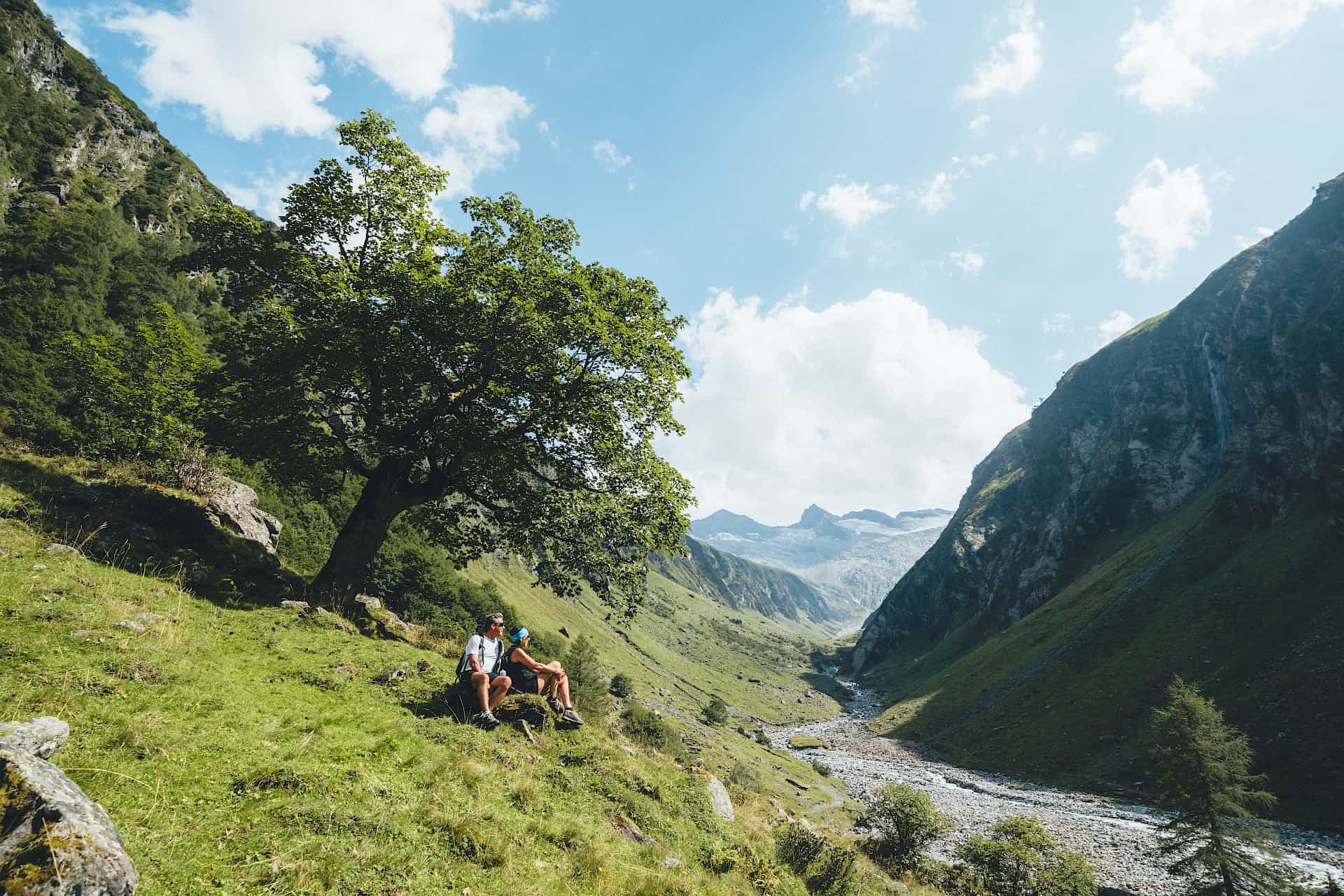 Turisté si užívají odpočinek v idylickém závěru údolí Vysokých Taur – obklopeni zelení, skalnatými stěnami a výhledem na ledovec uprostřed národního parku.