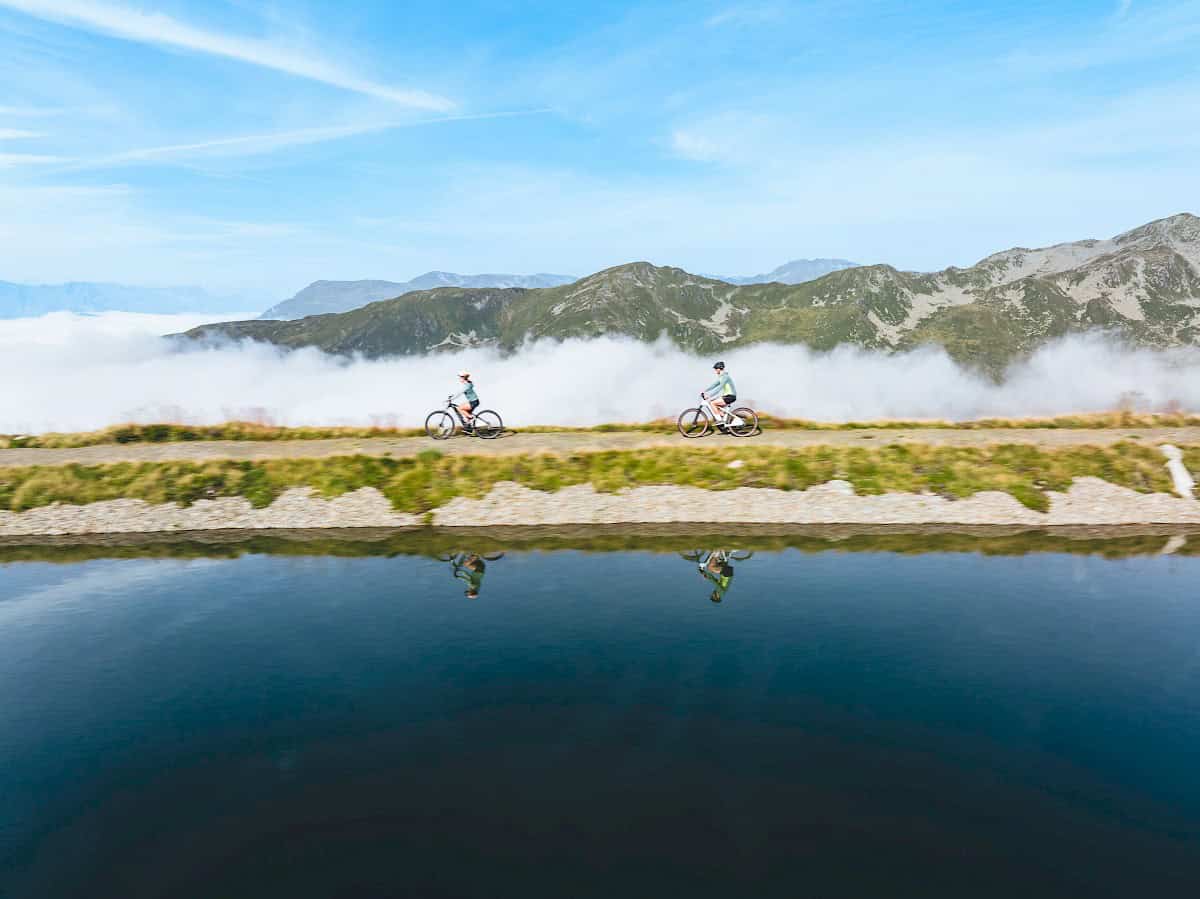 Zwei Radfahrer genießen eine Panorama-Tour entlang eines klaren Bergsees mit Blick auf die Kitzbüheler Alpen in der Wildkogel-Arena Neukirchen & Bramberg.