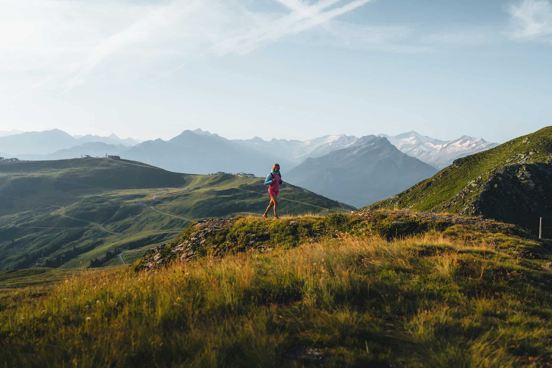 Žena putuje za časného rána po slunném horském hřebeni ve Wildkogel Areně – dechberoucí panorama, čerstvý horský vzduch a aktivní odpočinek při turistice ve Vysokých Taurách.