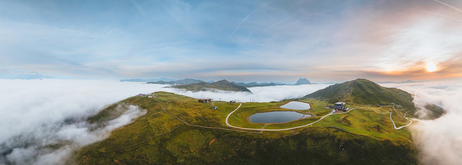 Východ slunce nad oblastí Wildkogel Arena s alpskými loukami, turistickými stezkami a mořem mraků – dechberoucí výhled v Národním parku Vysoké Taury.
