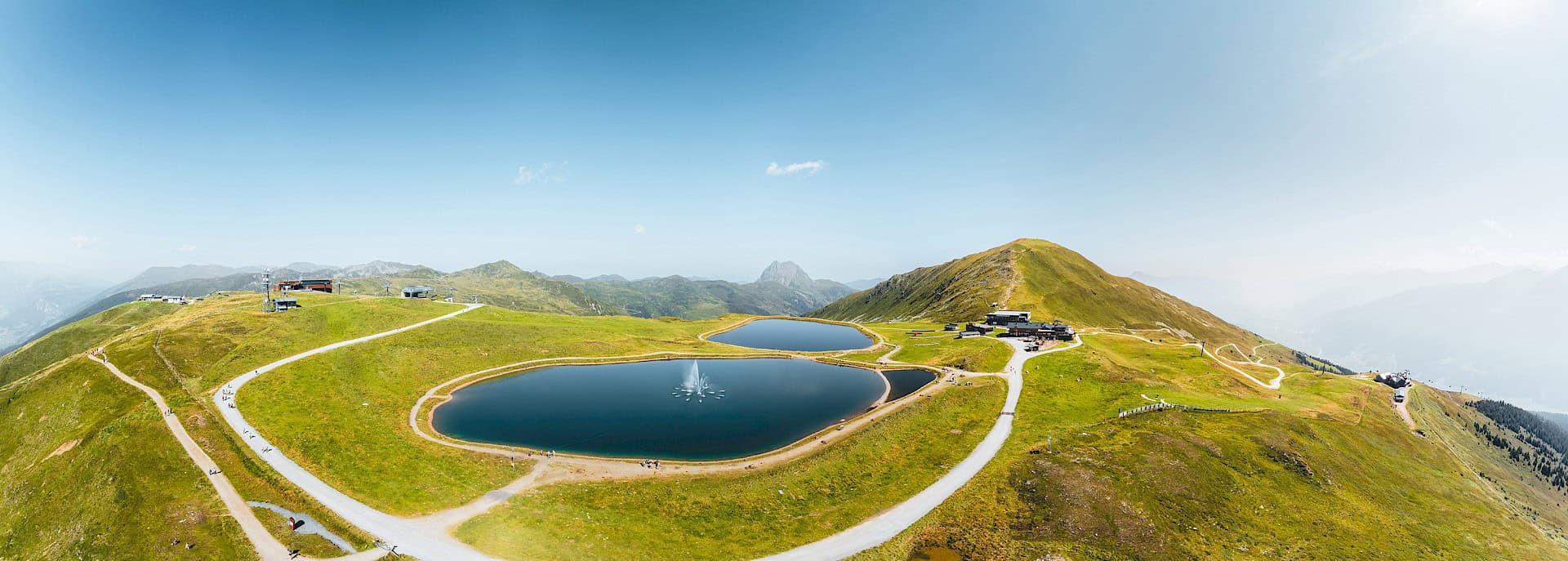 Panoramatický výhled na oblast Wildkogel Arena v létě s vodními nádržemi, turistickými stezkami a alpskou krajinou – ideální výletní cíl v pohoří Vysoké Taury.