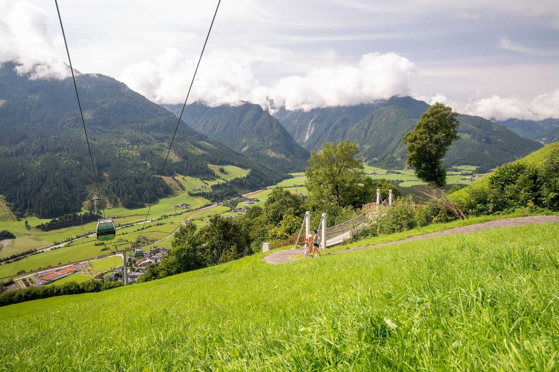 Maminka s dcerami jsou na cestě ke stezce „Adler Toni Weg“ – u vstupu poblíž prostřední stanice lanovky Wildkogel s výhledem do údolí.