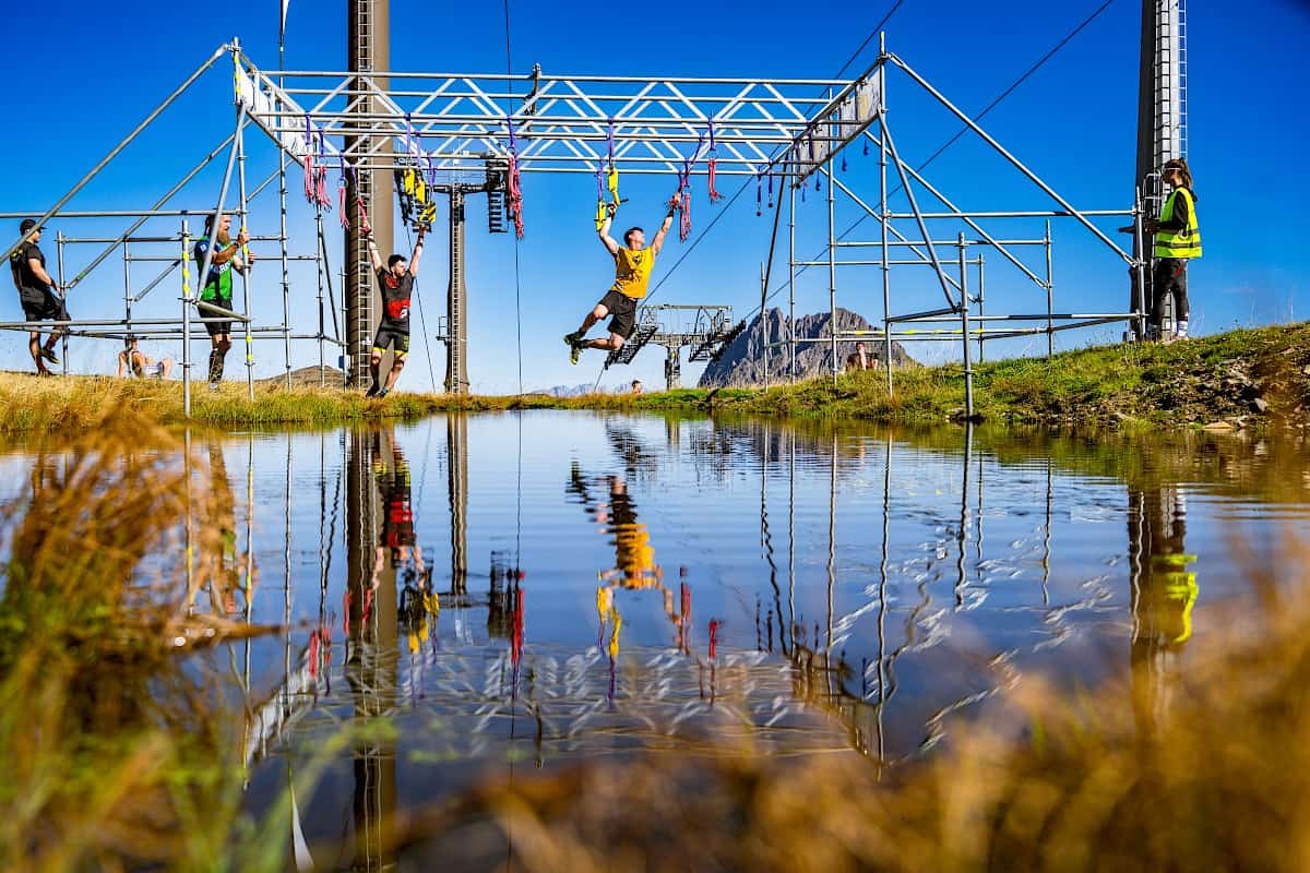 Teilnehmer des Predator Race überqueren ein Hindernis über dem Wasser – im Hintergrund der markante Große Rettenstein in der Wildkogel-Arena.