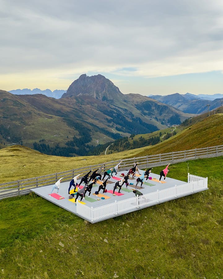 Teilnehmende der Bewegungswoche „Bergzeit – move & soul retreat“ machen gemeinsam Yoga auf einer Plattform mit Blick auf den imposanten Großen Rettenstein.