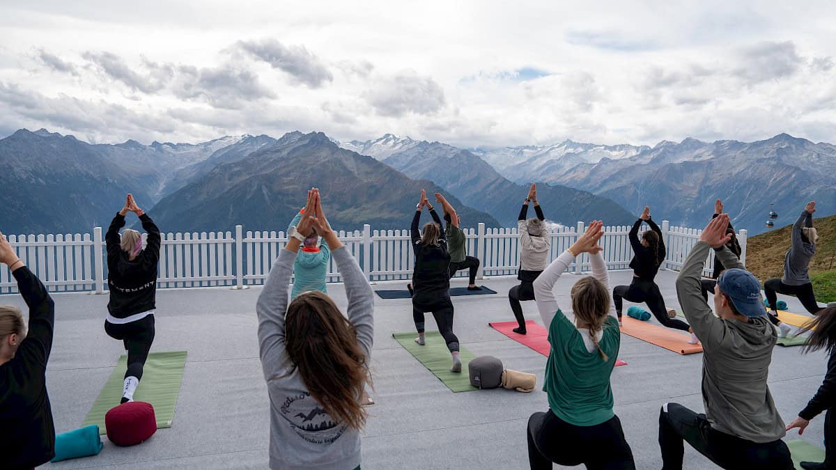 Yoga in luftiger Höhe mit Weitblick: Teilnehmer:innen der "Bergzeit – move & soul retreat" praktizieren achtsame Bewegungen auf einer Plattform mit atemberaubender Aussicht auf den Nationalpark Hohe Tauern.