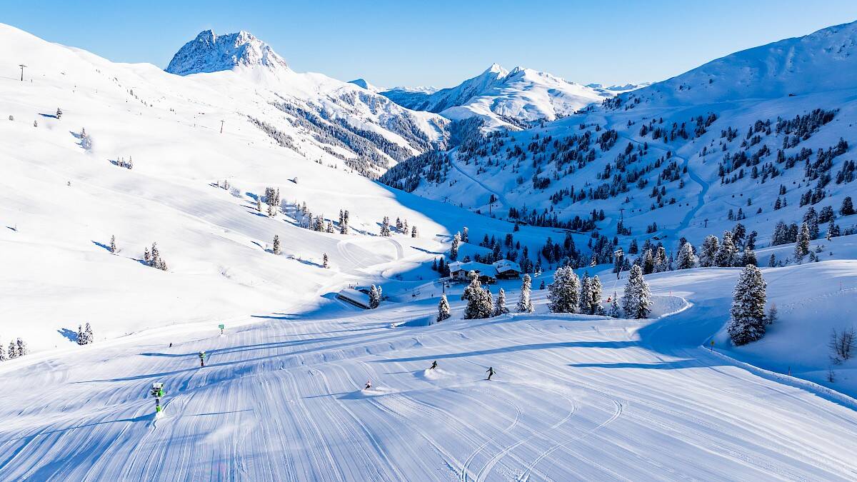 Weitläufige, frisch präparierte Pisten der Wildkogel-Arena mit Skifahrern vor der winterlichen Bergkulisse.