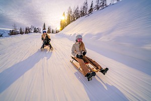Zwei Personen rodeln rasant die verschneite Strecke der längsten beleuchteten Rodelbahn der Welt in der Wildkogel-Arena hinab.
