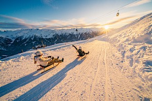 Rodler sausen bei Sonnenuntergang die längste beleuchtete Rodelbahn der Welt in der Wildkogel-Arena hinab.