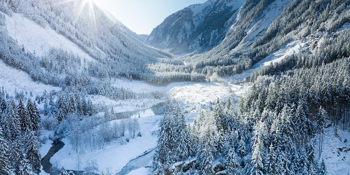 Winterliche Landschaft in Sulzau bei Neukirchen mit verschneiten Wäldern, Bergen und einem geschwungenen Fluss im Sonnenlicht. uk-cover