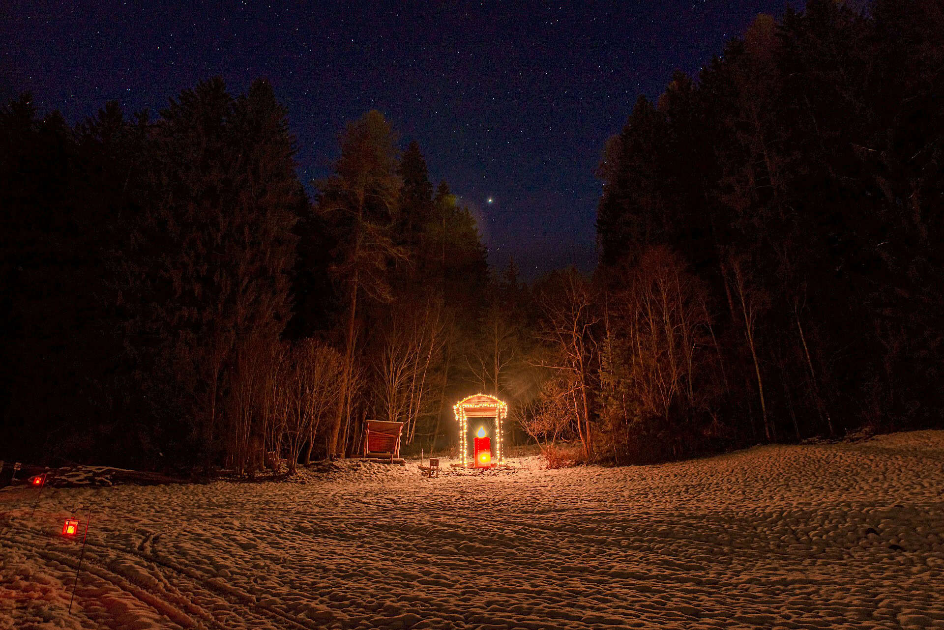 Große, warm beleuchtete Laterne am Laternenweg in Bramberg, umgeben von verschneiter Waldlichtung in der Nacht.