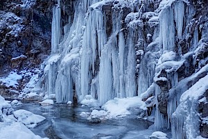 Gefrorene Eiszapfen beim Wasserfall mit verschneiten Bäumen und Bergen im Hintergrund