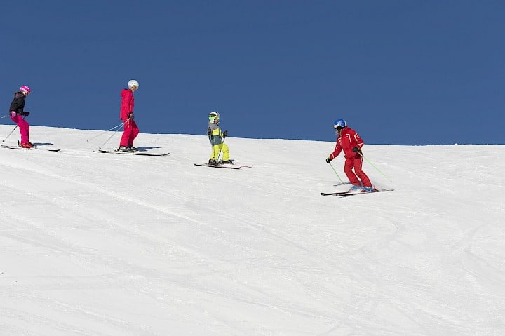 Lyžařský instruktor s dětmi na lyžařském kurzu ve Wildkogel Areně na slunečné sjezdovce pod jasně modrou oblohou.
