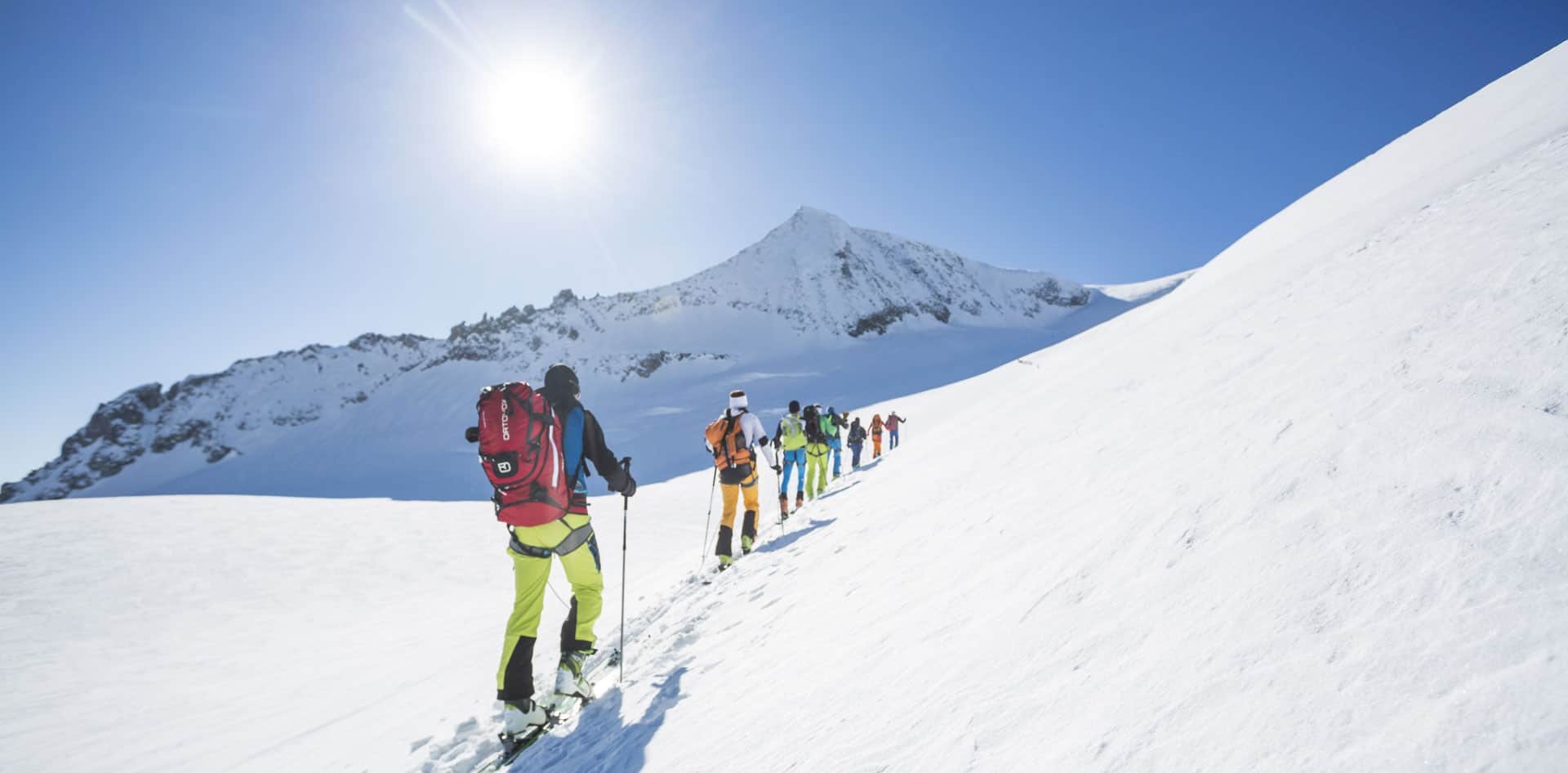 Skupina skialpinistů stoupá za slunečného dne na zasněžený Großvenediger – působivá skialpinistická túra ve Vysokých Taurách pro milovníky hor a přírody.