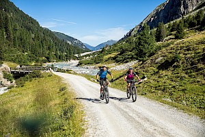 Zwei Mountainbiker genießen eine aussichtsreiche Radtour entlang eines klaren Gebirgsbaches im Obersulzbachtal im Nationalpark Hohe Tauern – Naturgenuss und sportliche Aktivität im Sommerurlaub in der Wildkogel-Arena.