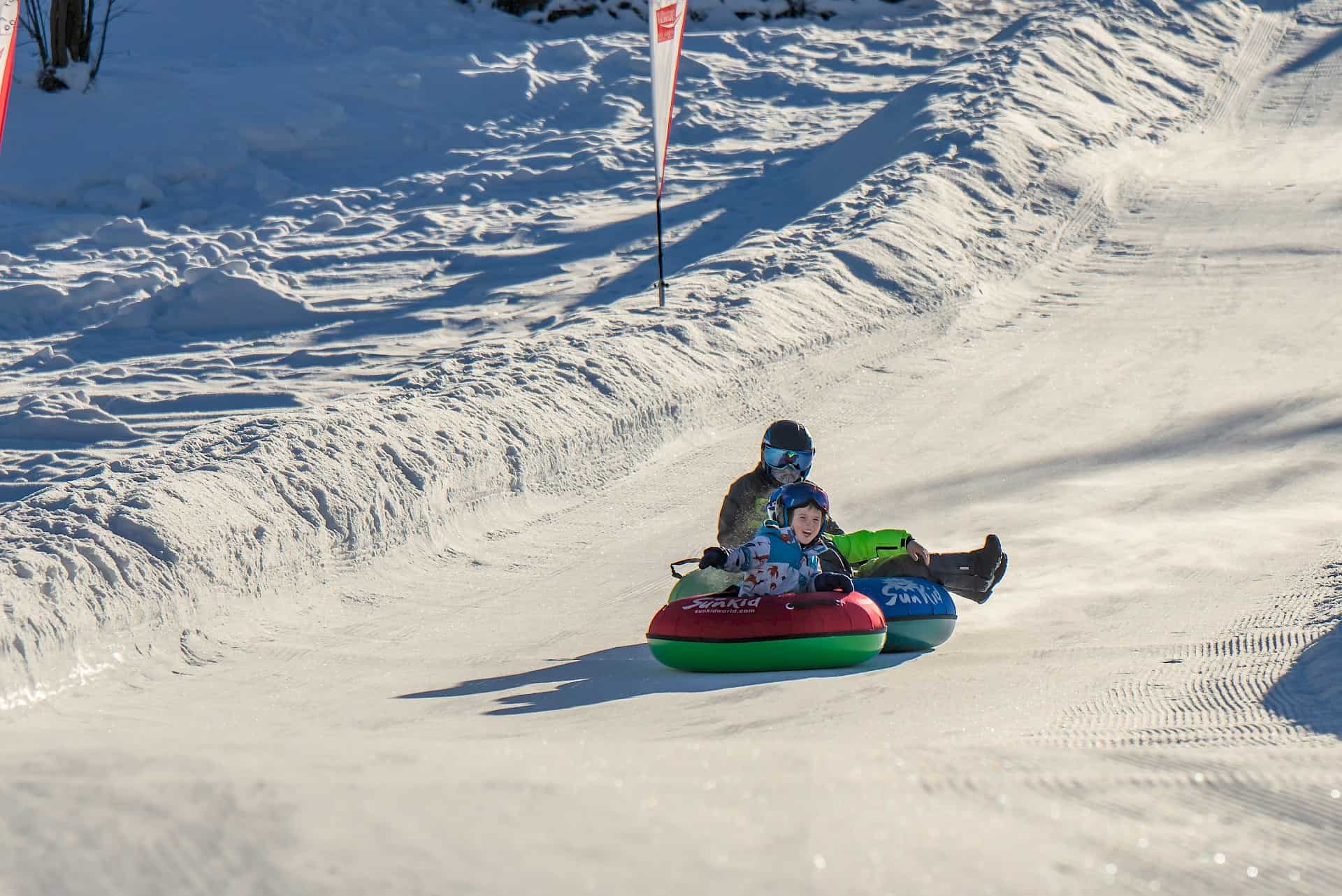Zimní zábava při snowtubingu v oblasti Wildkogel Arena – usměvavé děti a dospělí na upravené tubingové dráze za slunečného dne.