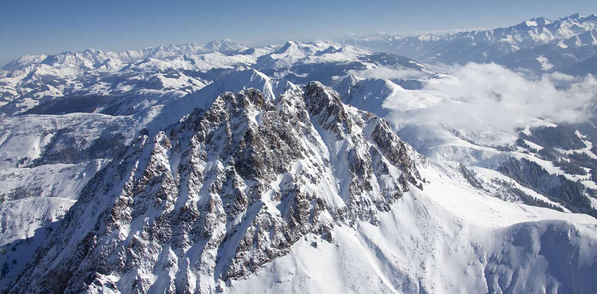 Atemberaubender Blick auf die schneebedeckten Gipfel der Alpen im SalzburgerLand. Die gezackten Felsformationen im Vordergrund ragen imposant in den klaren blauen Himmel, umgeben von einem weiten Panorama aus Tälern, Hügeln und weiter entfernten Bergketten.