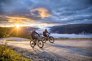 Zwei Mountainbiker erleben den Sonnenaufgang im Wildkogelgebiet, über dem nebelverhüllten Salzachtal.