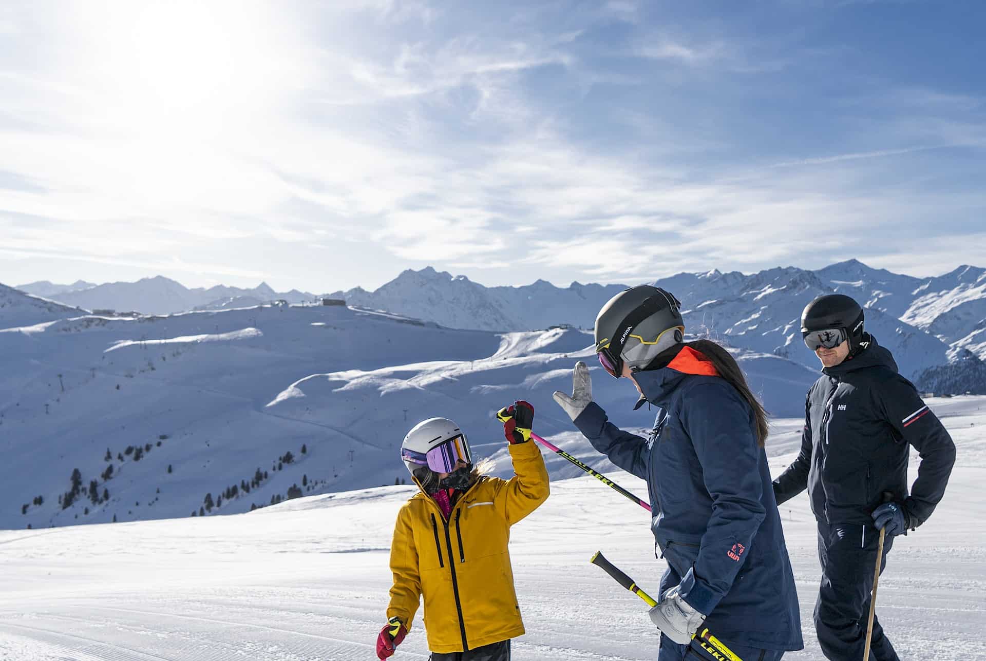 Lyžařka a dítě si dávají high-five na sjezdovce ve Wildkogel Areně za slunečného počasí, v pozadí zasněžené hory.