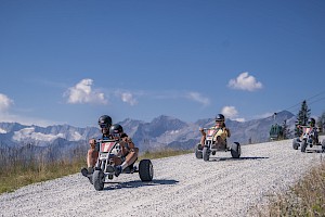 Familie fährt mit Mountaincarts auf der 4 km langen Mountaincart-Strecke in der Wildkogel-Arena hinab – rasante Outdoor-Aktivität für Groß und Klein mit Panoramablick auf die Gipfel der Hohen Tauern.
