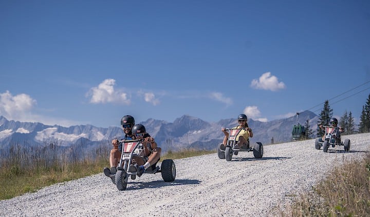 Familie fährt mit Mountaincarts auf der 4 km langen Mountaincart-Strecke in der Wildkogel-Arena hinab – rasante Outdoor-Aktivität für Groß und Klein mit Panoramablick auf die Gipfel der Hohen Tauern.